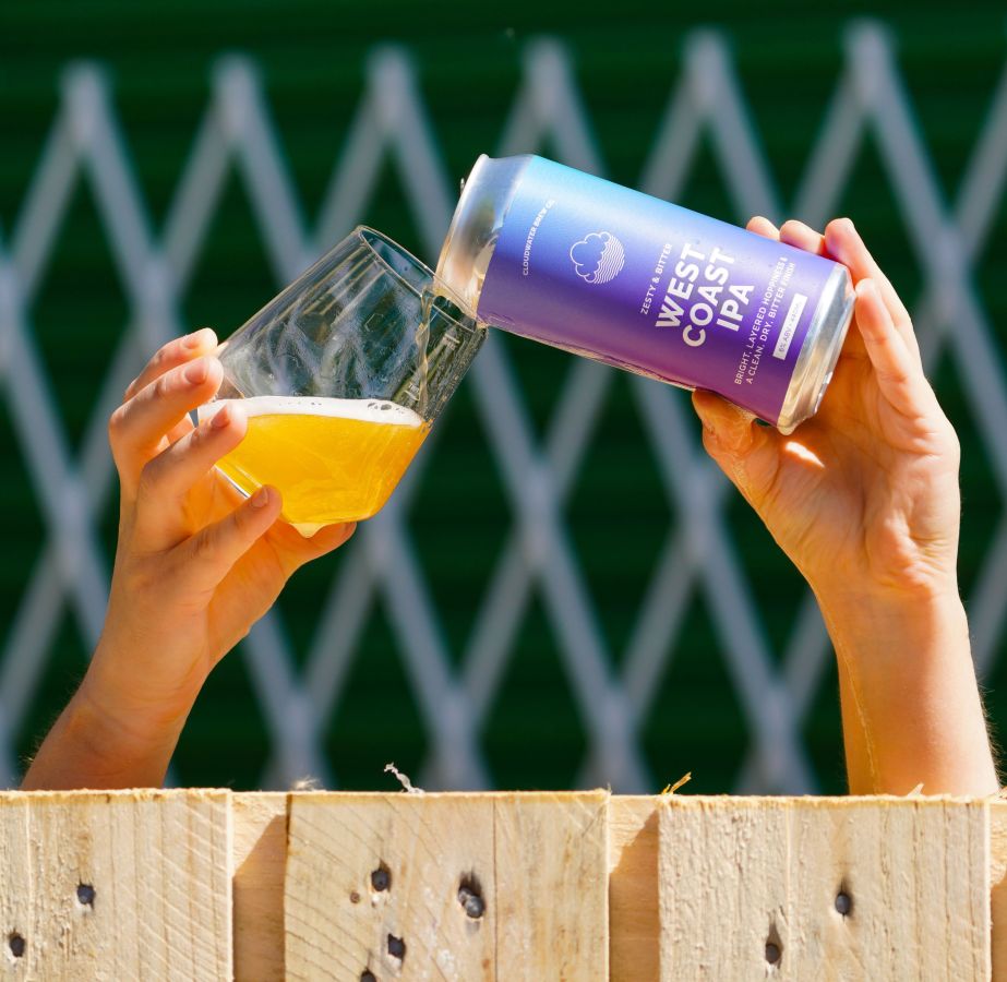 Photo of someone pouring a can of West Coast IPA into a glass overt the top of a wooden fence ©2020, Cloudwater Brew Co., Manchester, Greater Manchester