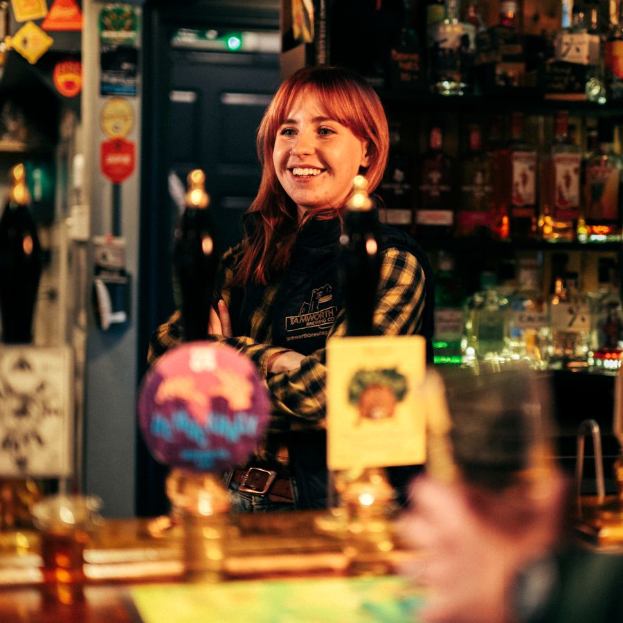Photo of a women smiling and working behind the bar at the Tamworth Tap © CAMRA
