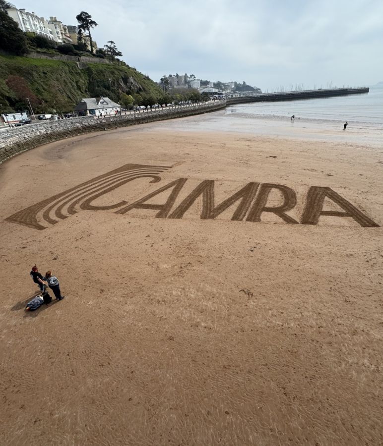 Photo of the CAMRA logo etched out on Torquay Beach © Alex Dewar, 2025
